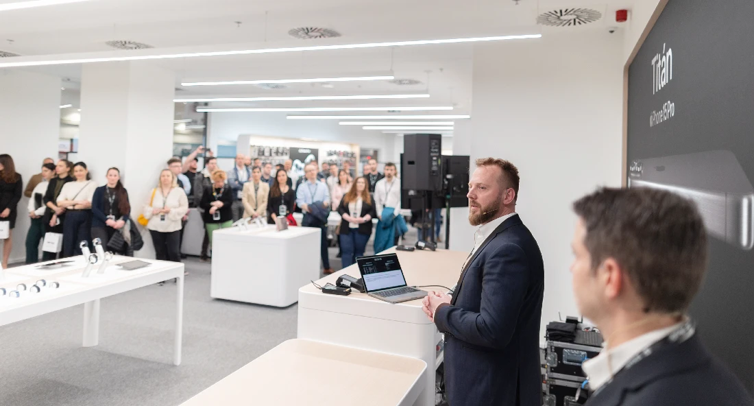 two men are seen addressing a group of people in a hi tech store 