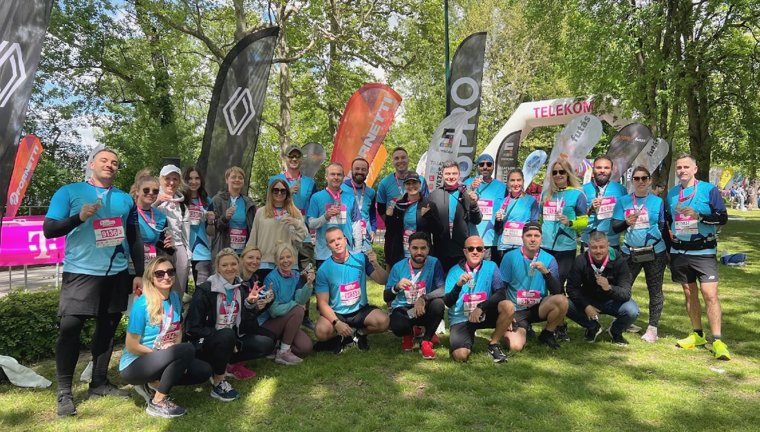 a group of runners in blue t shirts are seen resting after a half marathon race under the shade of trees in a park