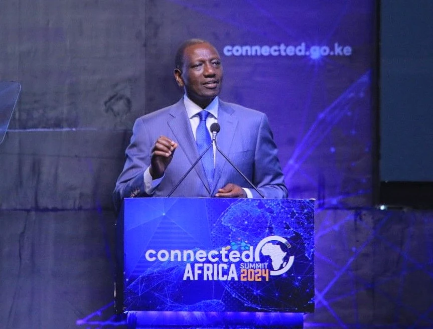 a man in a suit and tie is seen speaking from a dais in front of a presentation screen.