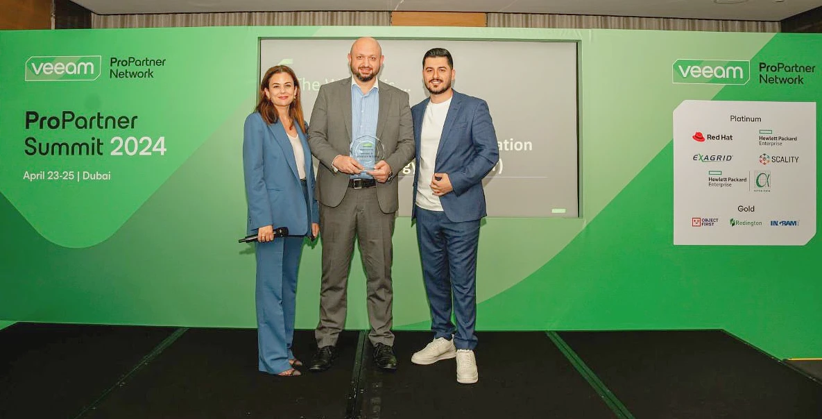 three people seen on a presentation stage as one of them is holding a glass trophy