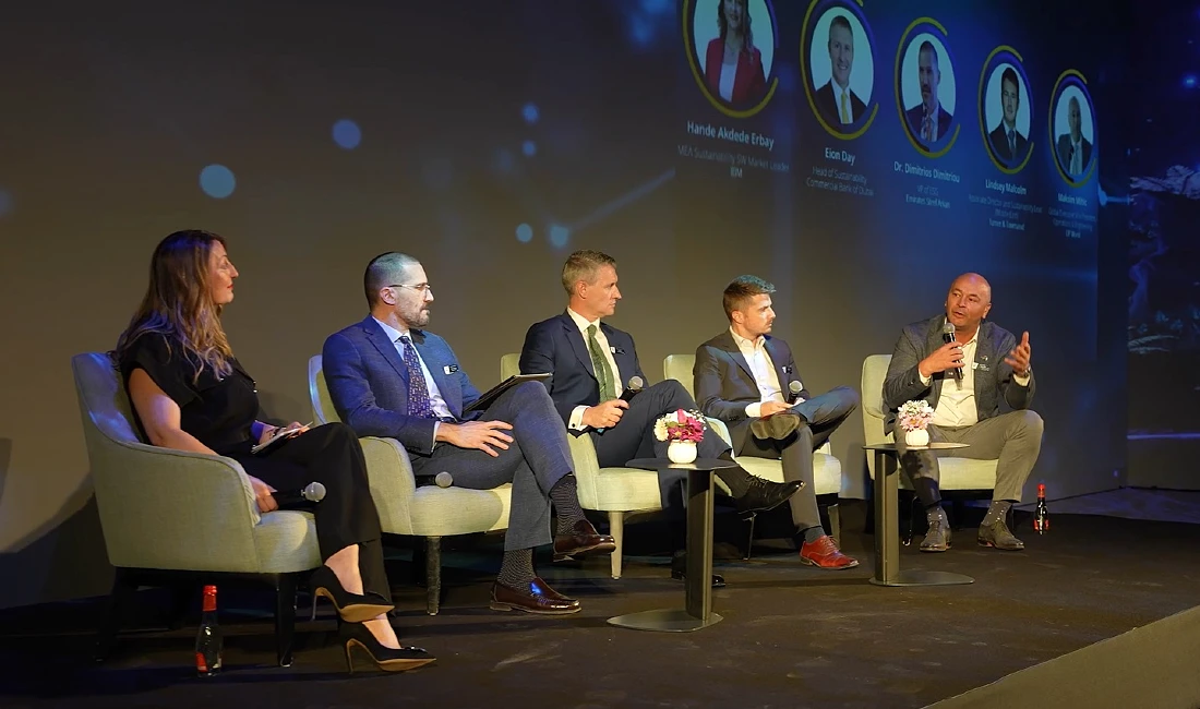 five people are seen sitting in chairs on a stage in a panel discussion.