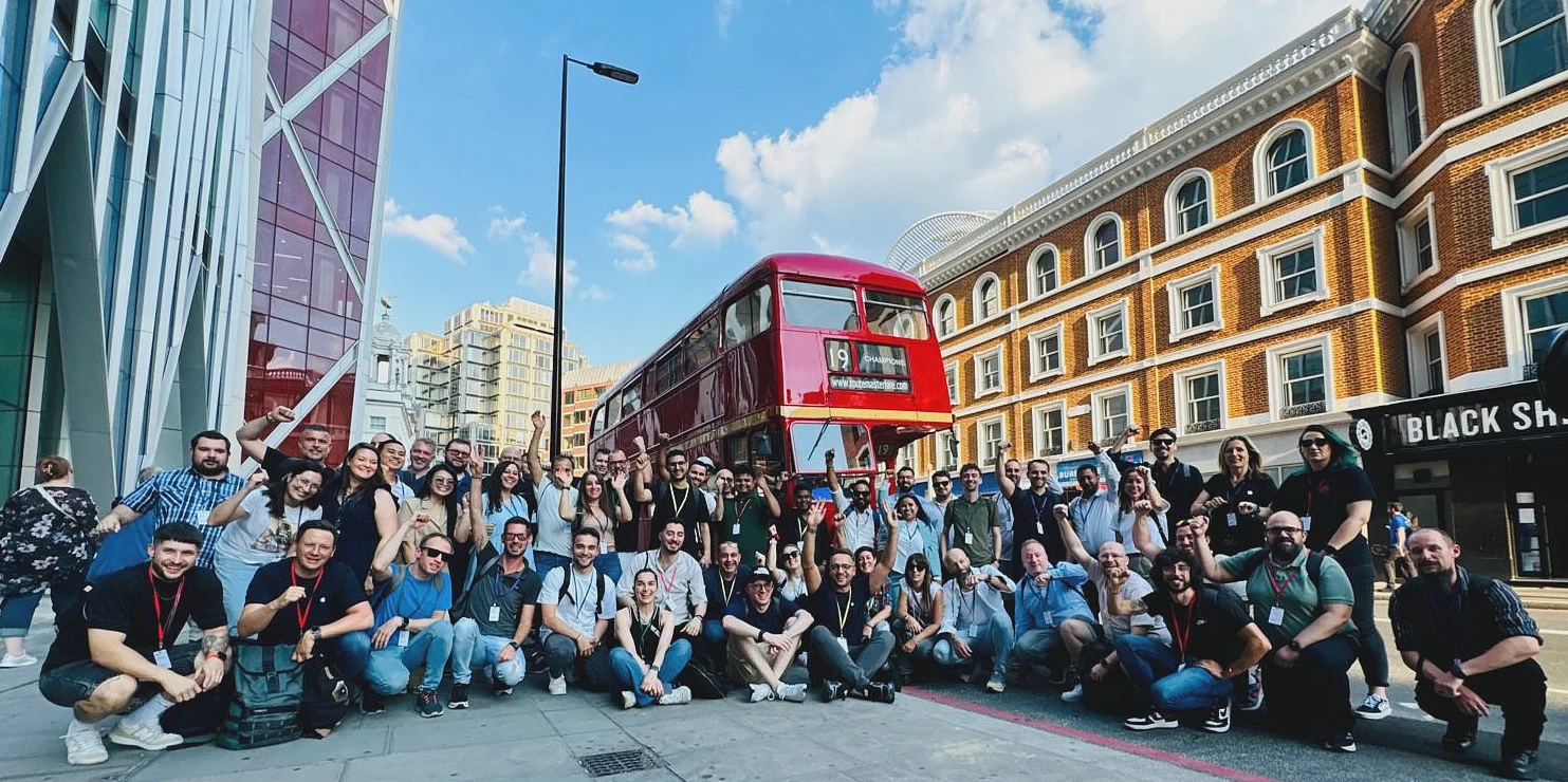 A large group photo taken outside in London with a red London bus in the backround. 