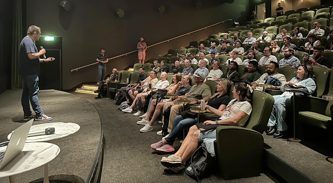 on the left, a man is talking into a mic and presenting to a group of people in an auditorium