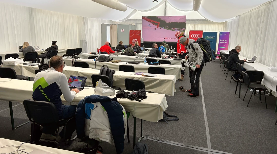 L’intérieur d’un centre de presse avec des rangées de tables et de chaises, et un grand écran au fond de la salle.