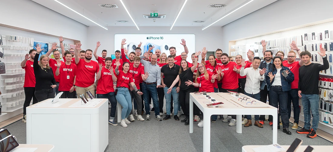 a group photo showing the iSTYLE Brno team in red t shirts waving and smiling at the camera