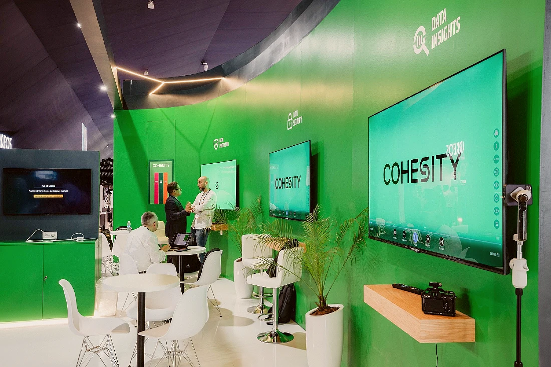 A booth at a hi tech exhibition - the walls of the booth are green and there are screens covering them. 