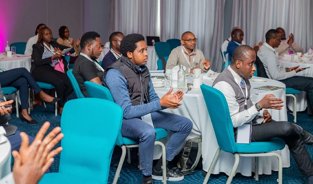 a view of the attendees at the event. People are sitting at tables and are seen applauding a presentation 