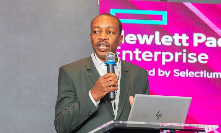 a man in a suit speaks into a mic to welcome people to the event