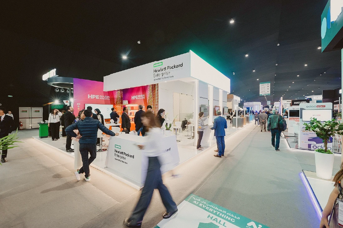 shows an exhibition stand at a hi tech event with people standing near and walking past 