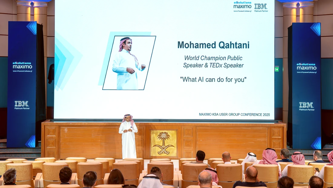 a man is seen speaking in front of a presentation screen in a large auditorium
