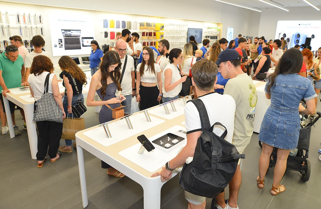 Intérieur d’un espace de vente high-tech avec de nombreuses personnes inspectant les appareils Apple exposés.