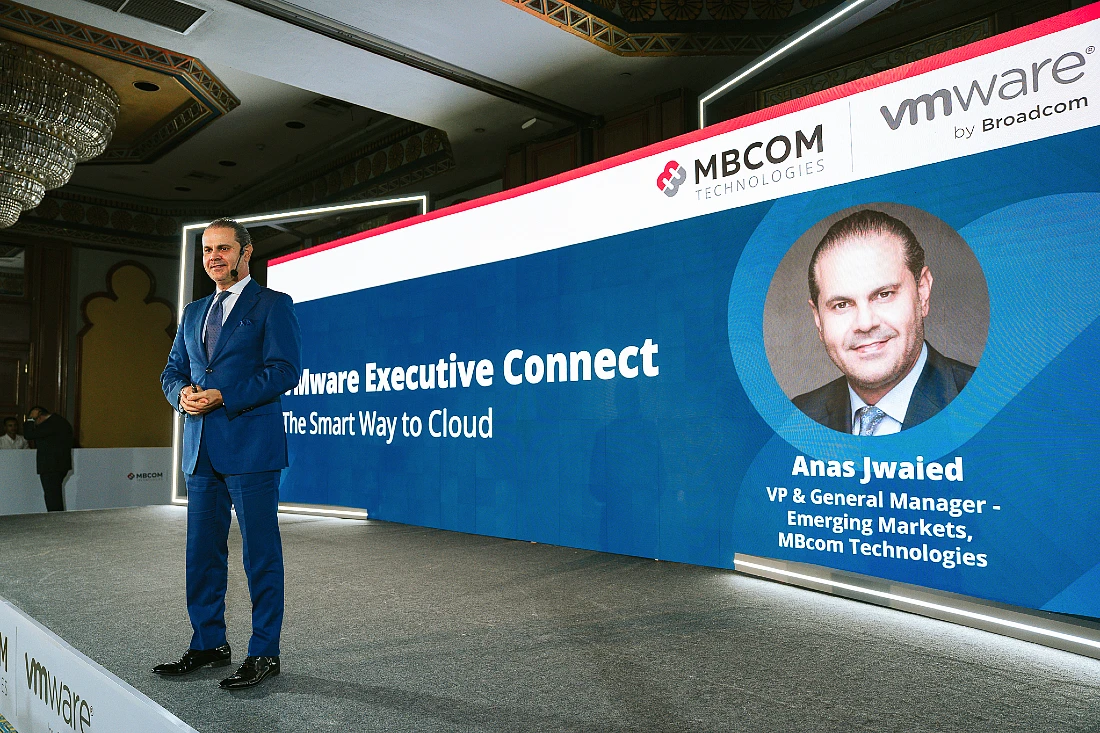 a man in a blue suit is seen in front of a large digital screen presenting to an audience