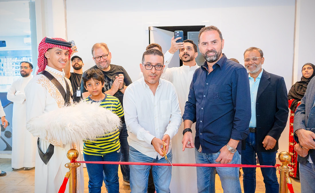 Un homme en chemise blanche tient une paire de ciseaux et coupe un ruban rouge pour inaugurer un magasin high-tech.