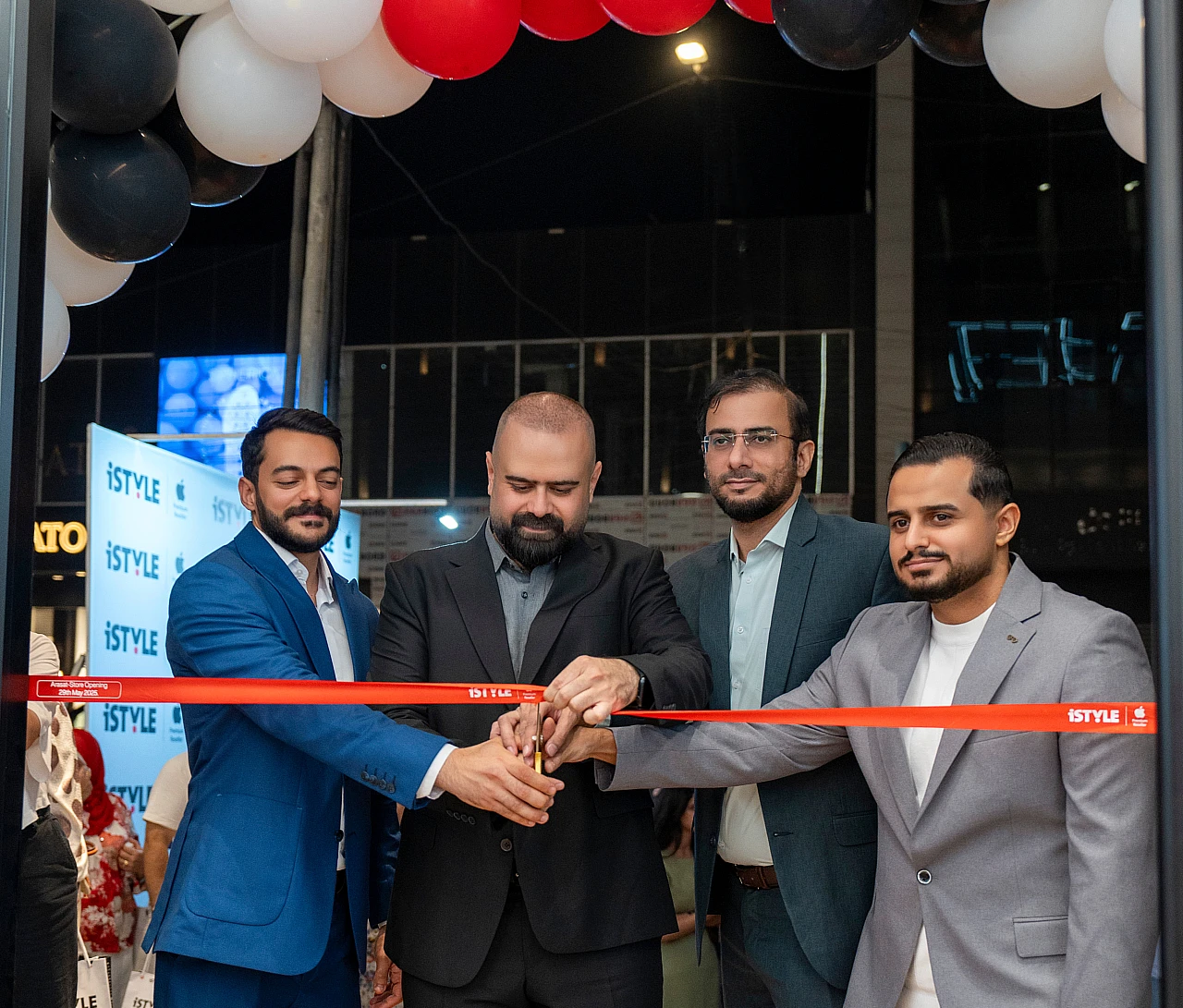 Four men in suits are seen cutting a red tape to open a hi tech store