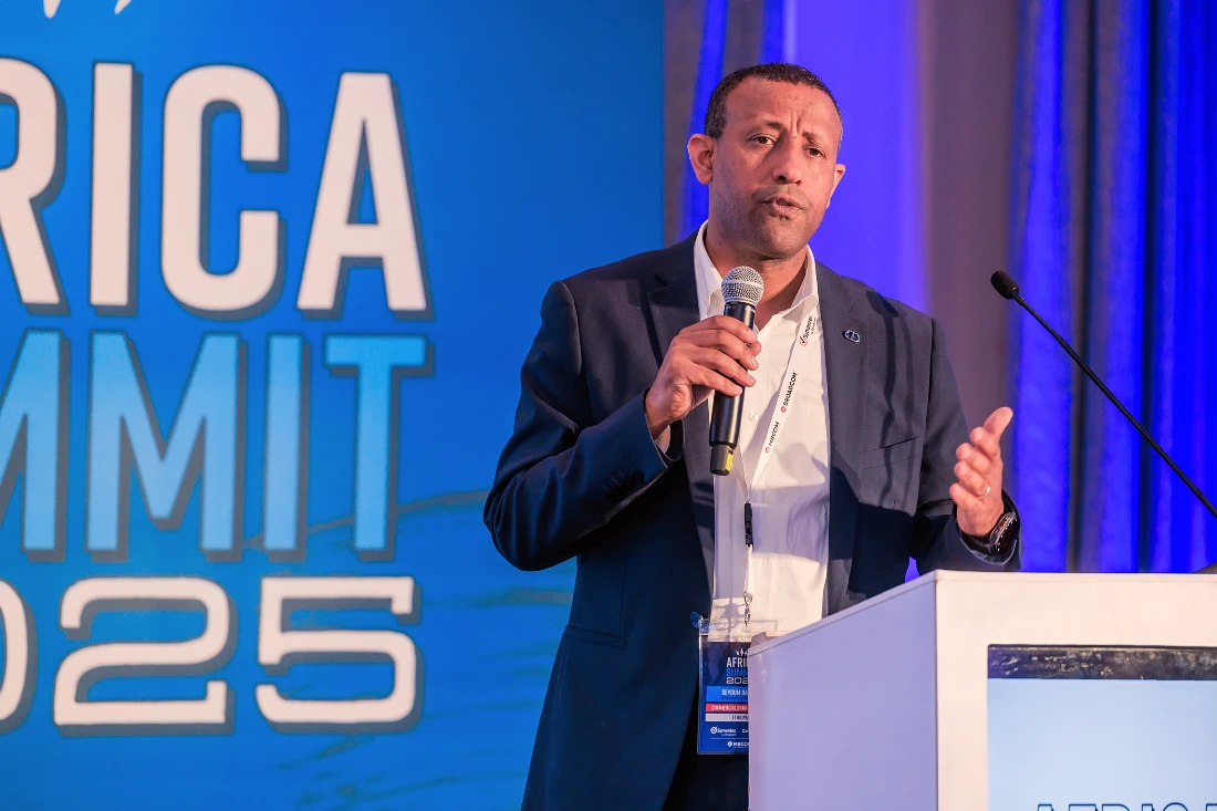 A man is seen in close up talking into a mic and gesturing with his hand at an IT event