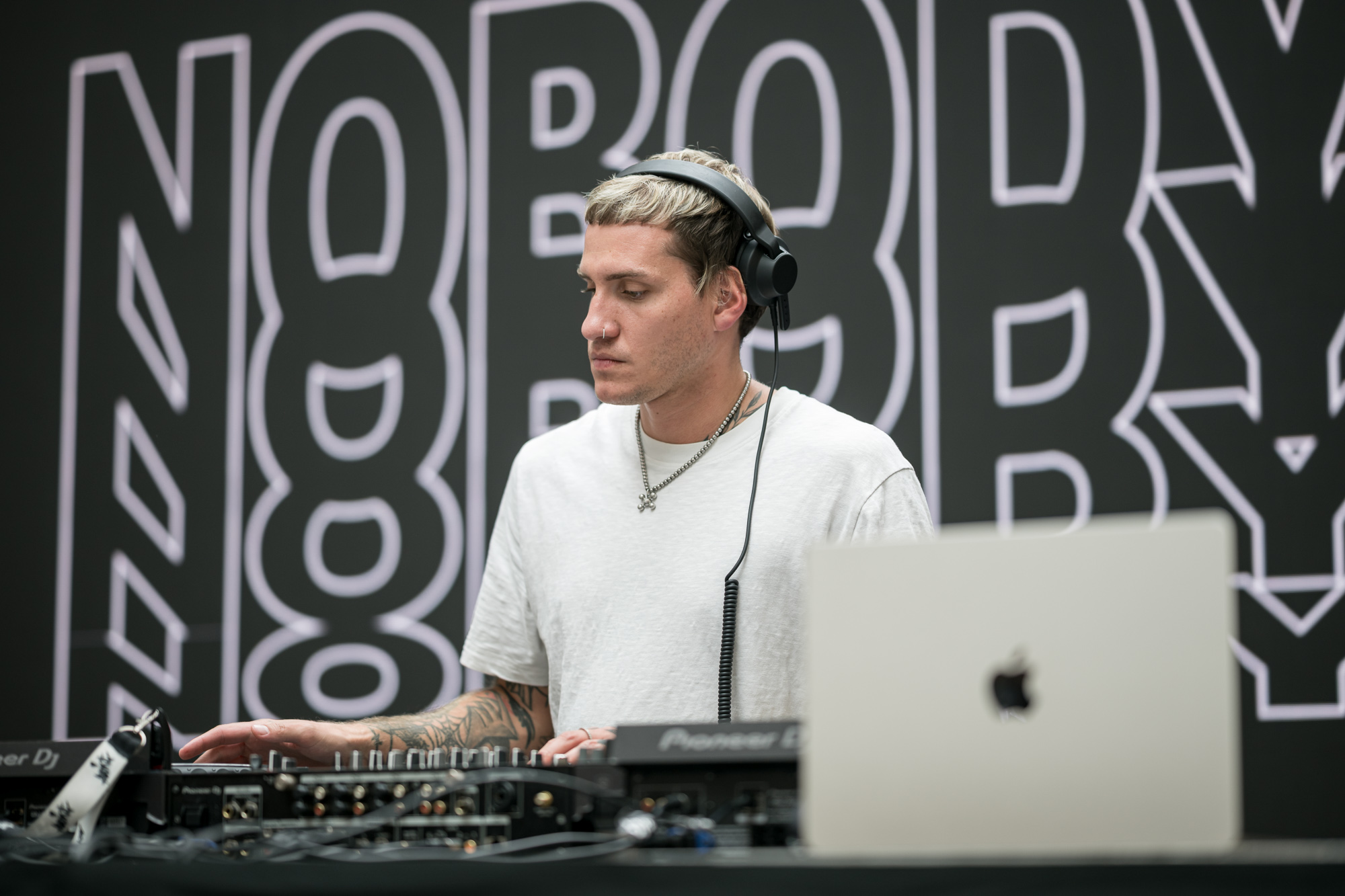 Un DJ joue de la musique lors de l’inauguration d’un magasin high-tech. Il porte des écouteurs et un ordinateur portable Apple est au premier plan.