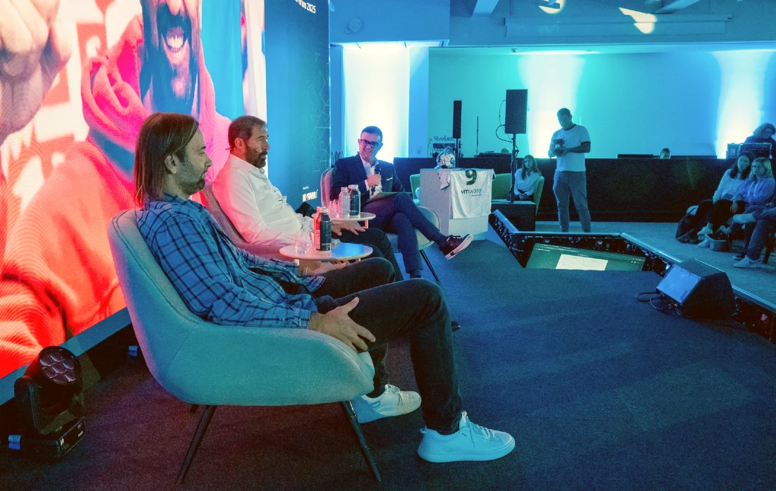 two men are seen sitting in front of a digital screen with a third man interviewing them 
