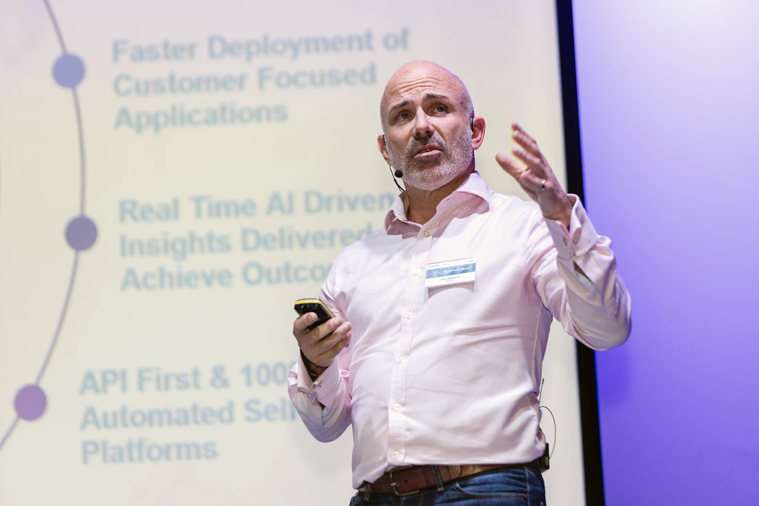 a man in a shirt speaks to an audience with a digital screen in the background
