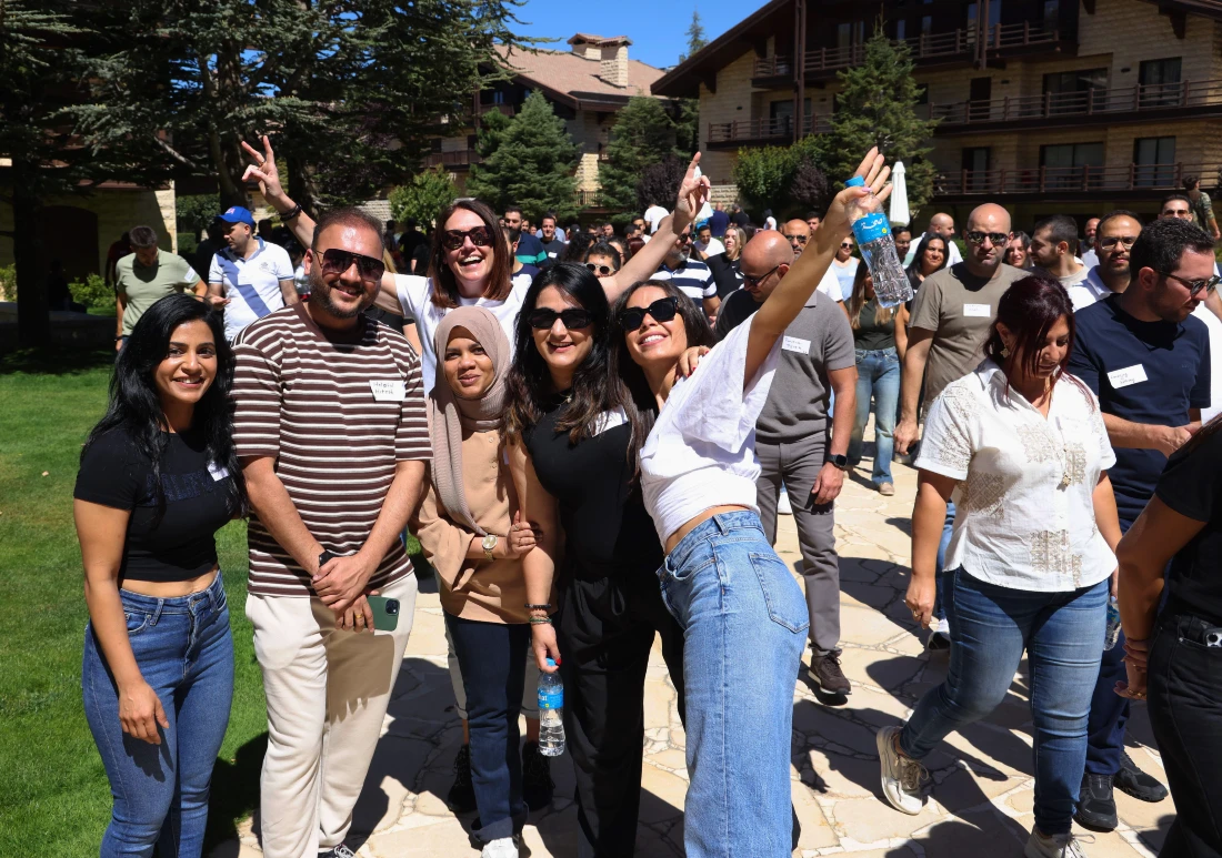 A group of people outdoors in casual clothes smile and wave at the camera