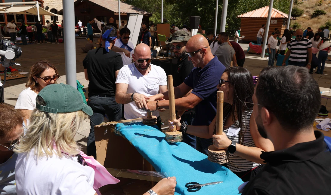 six people sit at a table outdoors and work together to make a Roman chariot out of wood and cardboard
