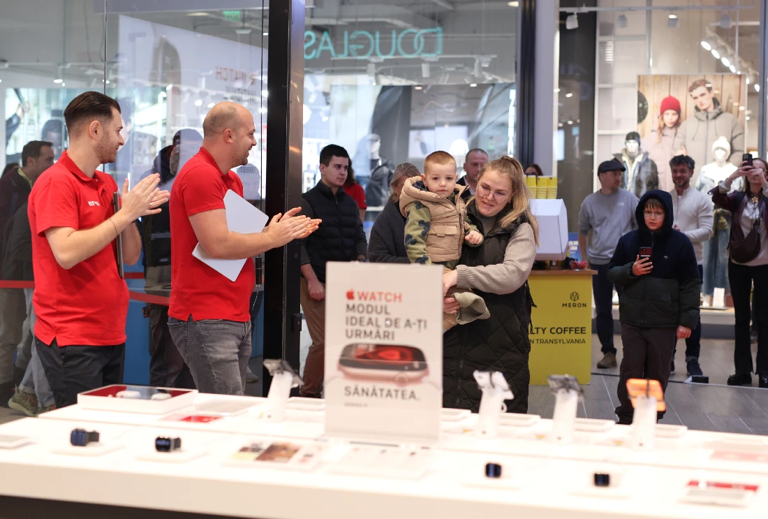 Two store team members clap as a woman and young child enter a hi tech store as it opens for the first time. 