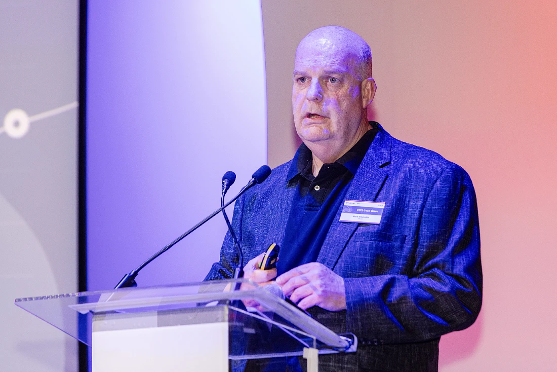 A man in a suit speaks at a rostrum at a hi tech event