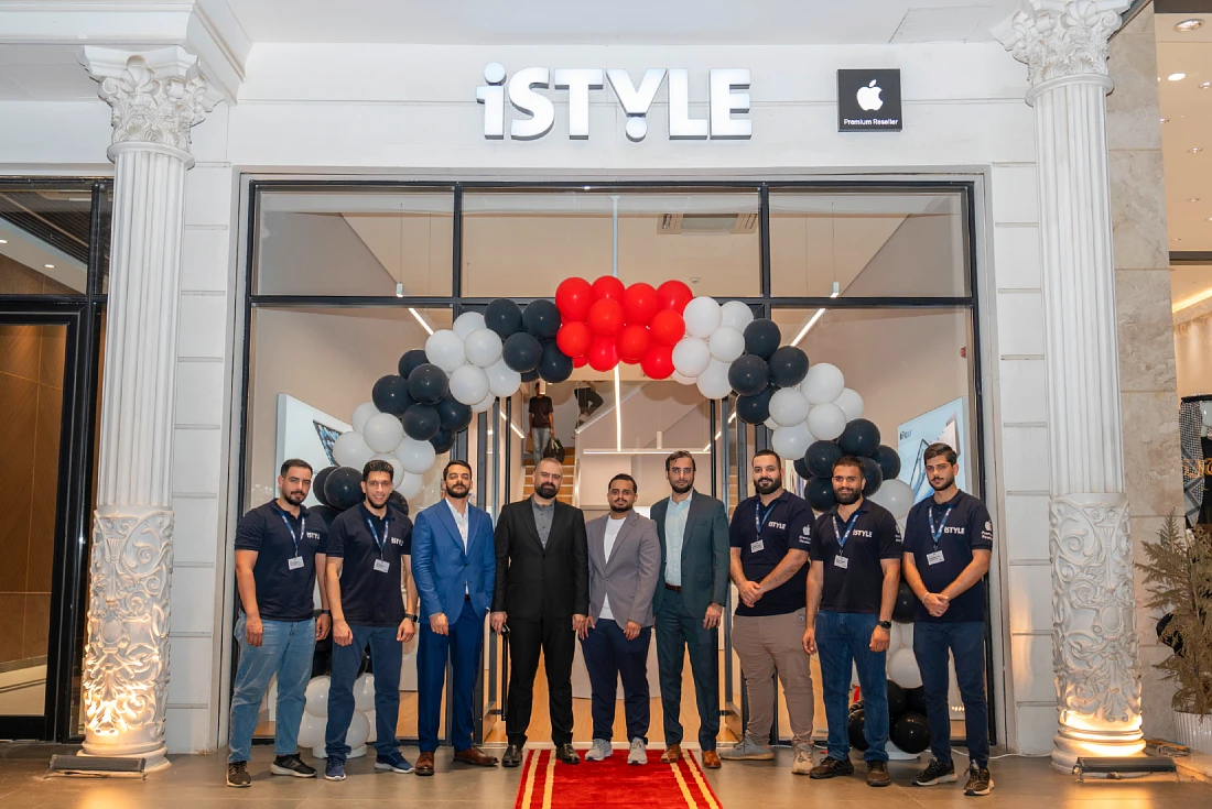 Nine men are seen out side the front of a hi tech store with black, red and white balloons hanging from the frontage.