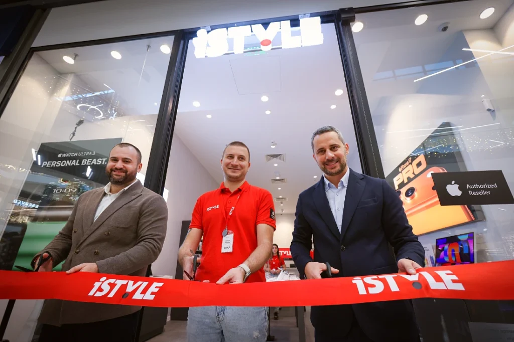 Three men stand behind a large red tape and prepare to cut it with scissors outside a hi tech store