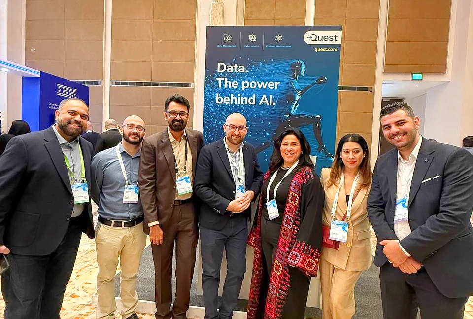 Seven people in a group photo at a hi tech event. Behind them is a display board with the phrase Data - the power behind AI