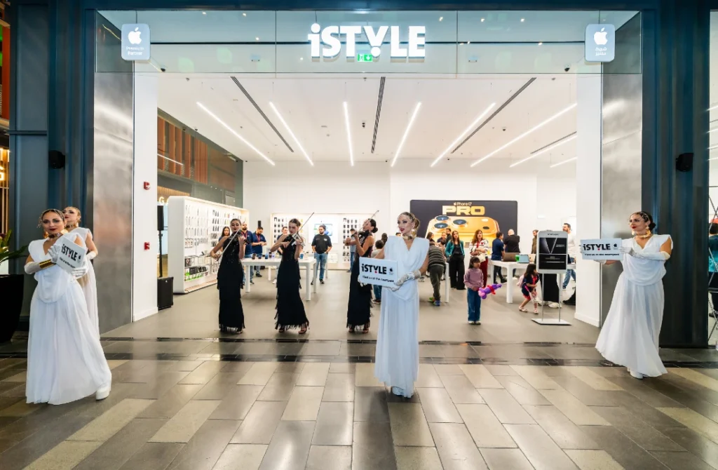 Exterior view of a hi tech shop at night with women wearing etherial dresses welcoming people to an opening event
