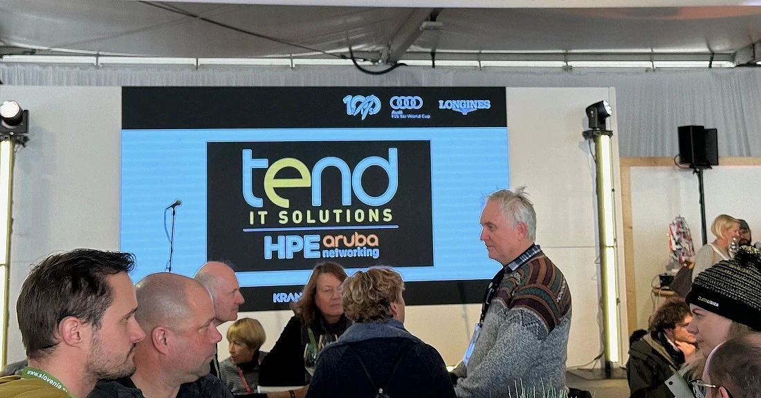 Des personnes vues à l’intérieur d’une tente des médias, avec un grand écran derrière elles. 