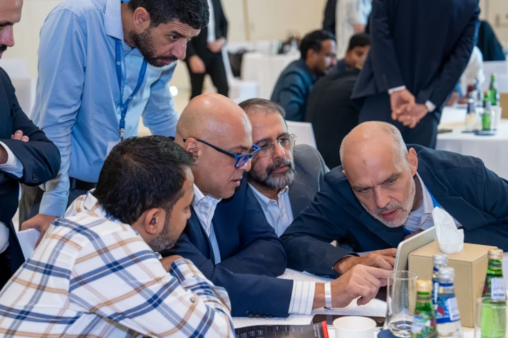 A group of men are seen clustered around a laptop staring intently at the screen as they try to solve a cyber security attack