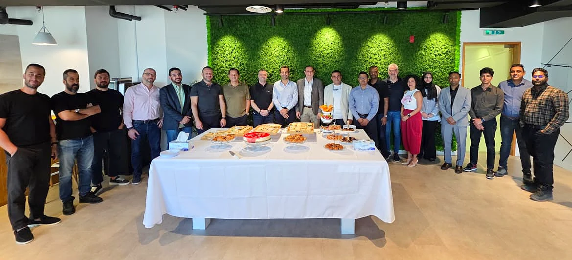 a group photgraph with people arranged around a table with celebration snacks on it 