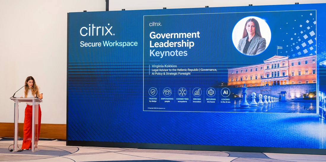 A woman presents at a hi tech event with a large blue screen to her left