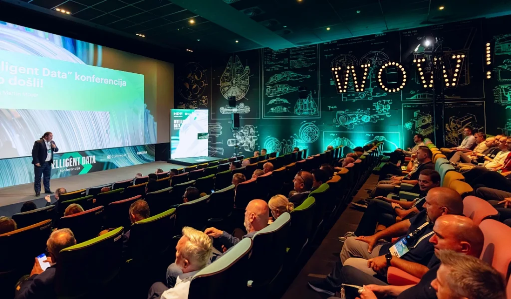 Un homme accueille les participants à un événement high-tech, s'exprimant depuis la scène d'un auditorium.