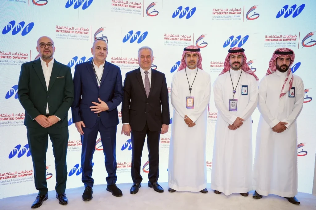 Six men are seen in a group photograph at a hi tech event. The background is a screen with company logos on it. 