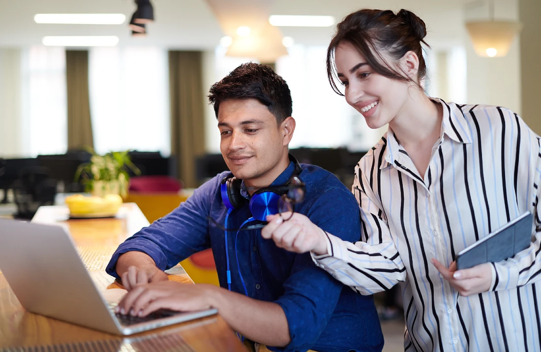 A man and a woman are both looking at the screen of a laptop