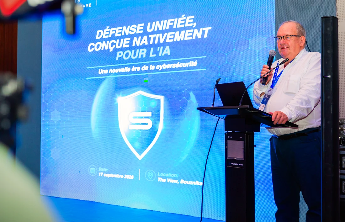 a man speaks into a mic at a hi tech event with a blue screen projected next to him.