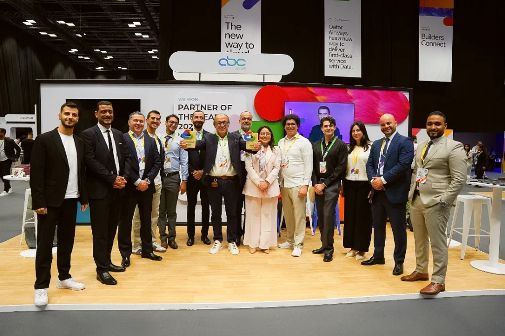 A team of people are seen at a hi tech event with a figure in the centre holding two award trophies.